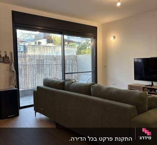 סלון מעוצב עם ריצוף פרקט בגוון עץ טבעי וספה ירוקה